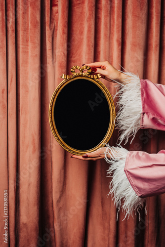 Woman's hand in nightgown holding vintage black hand mirror against pink curtains