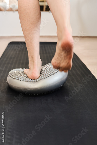 Konstfotografi Close view of bare feet and lower legs pressing textured balance cushion on blac