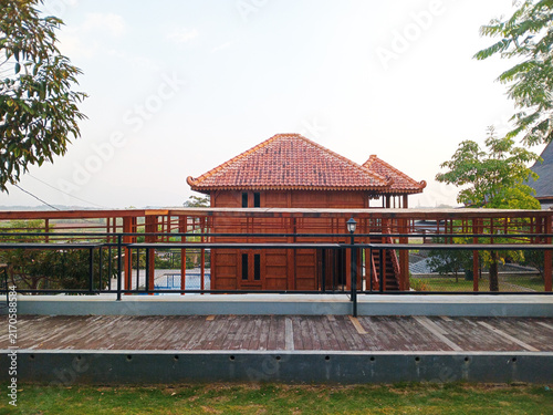 Wooden building featuring a classic terracotta roof, surrounded by a modern wooden deck and green grass, creating a relaxing outdoor scene
