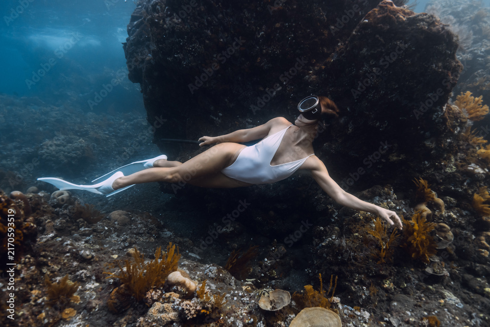 Fototapeta premium Woman freediving in white swimsuit above a coral reef in blue sea.