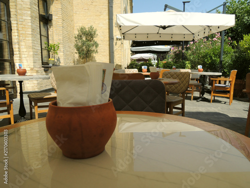 Clay Pot with Napkins on Table at Empty Outdoor Cafe in Hot Sunny Day 

