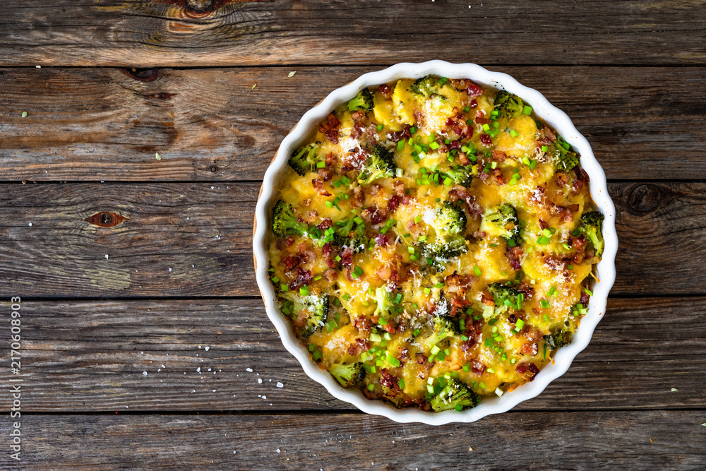 Obraz premium Potato broccoli casserole - baked potatoes with broccoli, cheddar cheese and smoked bacon on wooden table. Top view