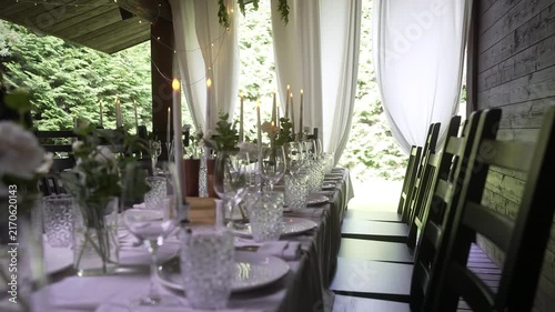 Rustic porch dining table with lit candles and crystal glassware under sheer curtains, with dining, table, candle, glassware detail, showing crystal, plate, napkin cutlery context