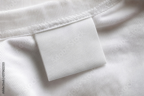 Blank white woven clothing label mockup sewn into white cotton t-shirt collar. Minimalist fabric neck tag template with copy space for apparel branding.