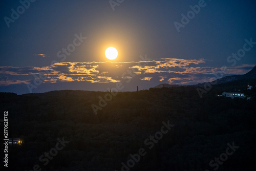 Fotografía Majestic bright yellow full moon rising over dark mountain silhouettes and drama