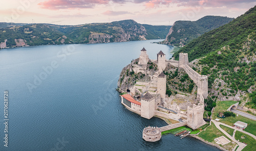 Foto Aerial view of a medieval fortress Golubac rising from a river gorge at dusk, bathed in soft pink twilight light