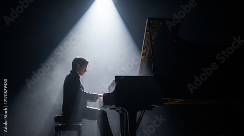 Solo musician performing on piano under dramatic spotlight  