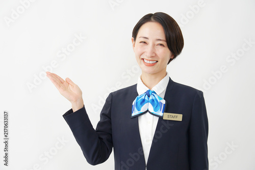 左側を手のひらで指すミドル女性スタッフ　白背景