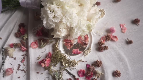 Bridal bouquet and ornate mirror with rings as petals settle on draped fabric, with bridal, bouquet, white, flower detail, showing ribbon, mirror, ring,wedding context