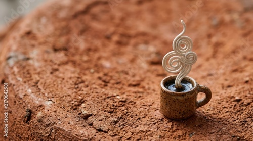 Miniature coffee cup with steam on brown texture.