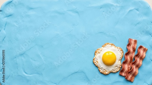 Miniature fried egg and bacon on blue background.