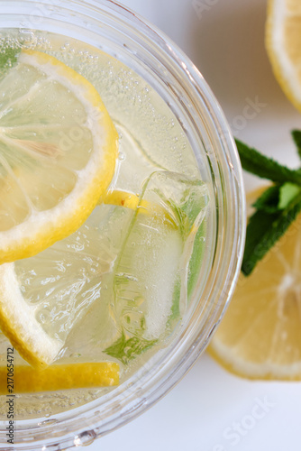 A vertical macro close-up shot from above showing ice, fresh lemon slices, and sparkling bubbles in a clear takeaway drink cup for beverage marketing, branding, and summer ad campaigns.