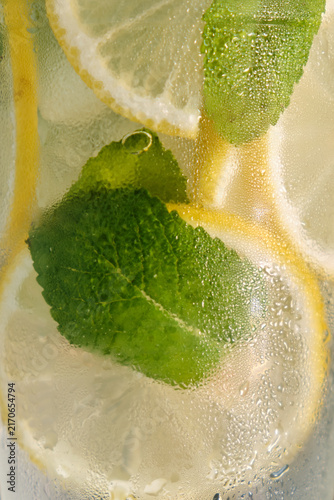 A horizontal macro close-up shot of a frosty glass filled with cold lemonade, ice, lemon slices, and fresh mint leaves for commercial beverage branding and summer advertising campaigns.