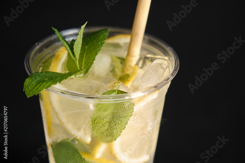 A horizontal close-up shot of a clear takeaway cup with cold iced lemonade, green mint leaves, and an eco straw on a dark background for beverage branding and cafe promotions.