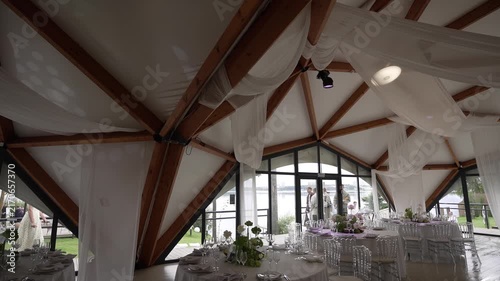 Interior event pavilion with exposed timber trusses, sheer drapery, and guests gathering near arched waterfront doors, with interior, pavilion, truss, beam 