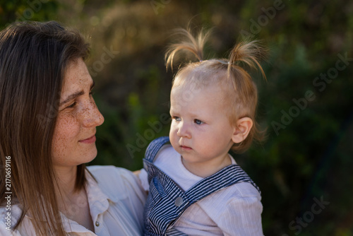 Mother holding her baby daughter with freckles and pigtails in soft natural light