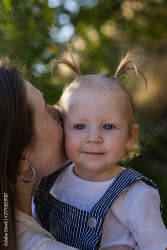 Fotografie Mother's gentle kiss on her child's cheek in a sunlit outdoor setting