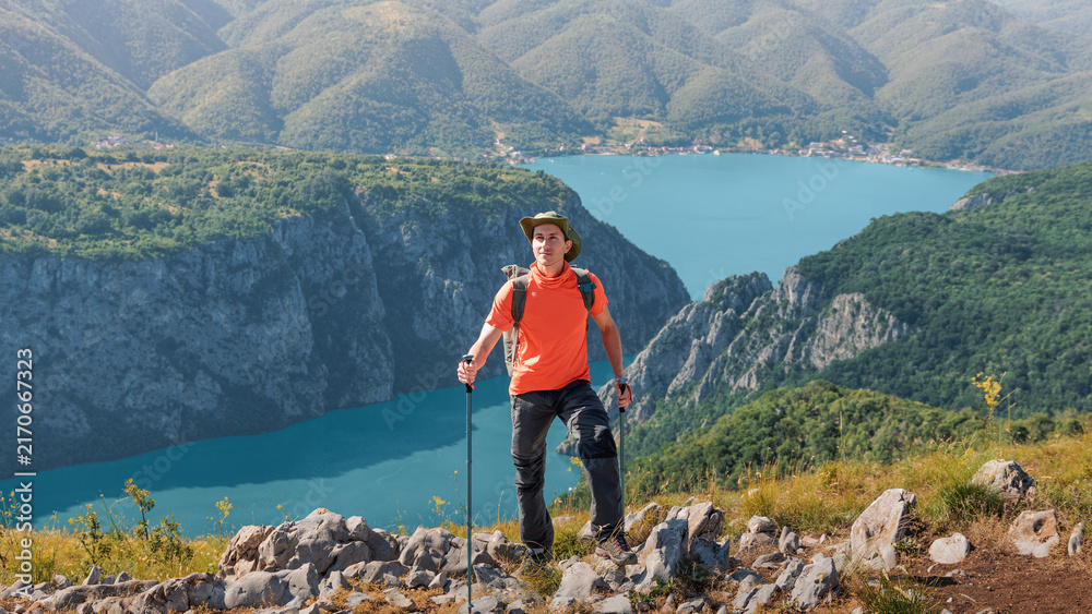 Naklejka premium Hiker with backpack and trekking poles standing on a viewpoint, enjoying a panoramic view of the Danube Iron Gates river canyon in Djerdap park