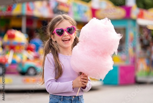 Happy little girl with pink cotton candy at a funfair