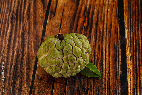 Cuadro en lienzo Green custard apple on rustic wooden surface with single leaf
