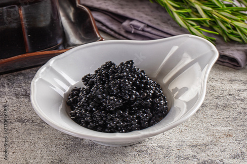 Photography Black caviar in white ceramic bowl with rosemary and dark napkin on stone surfac