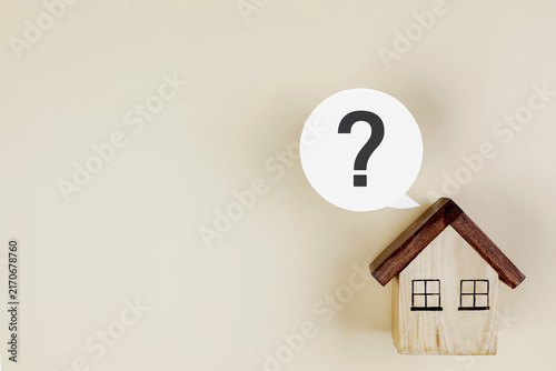 Small wooden house model with question mark speech bubble on cream background with copy space. Concept of real estate questions, home loan decision, house buying advice, and property search.