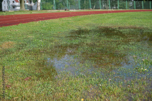 Athletics track after heavy rain with flooded grass, making outdoor training difficult in autumn