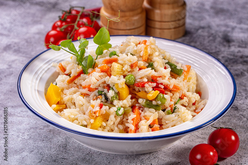 Фотография Bowl of basmati rice mixed with colorful vegetables on textured gray surface