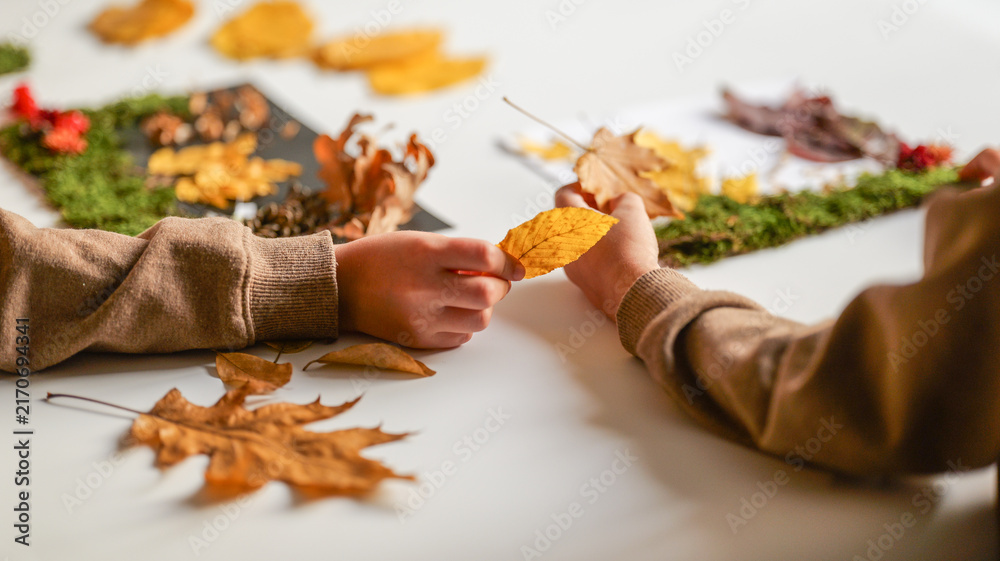 Naklejka premium Children's hands creating autumn nature crafts with leaves and moss