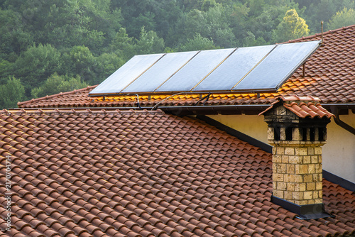 Aerial view of solar panels on the tiled roof of the House of Mijaks Ethno Restaurant, with a stone chimney and lush forest surroundings in Mavrovo, Municipality of Mavro, North Macedonia.