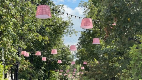 Outdoor string lights with pink lampshades hanging in a lush green park, creating a festive atmosphere