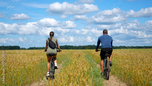 Foto Rear view of a man and woman in athletic wear on a bicycle trip, riding along a countryside route in a vast wheat field during a peaceful summer weekend