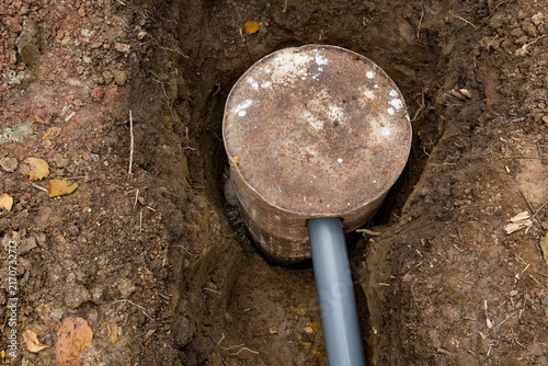 Grey PVC wastewater pipe connected to a buried rusty metal barrel acting as an improvised septic tank
