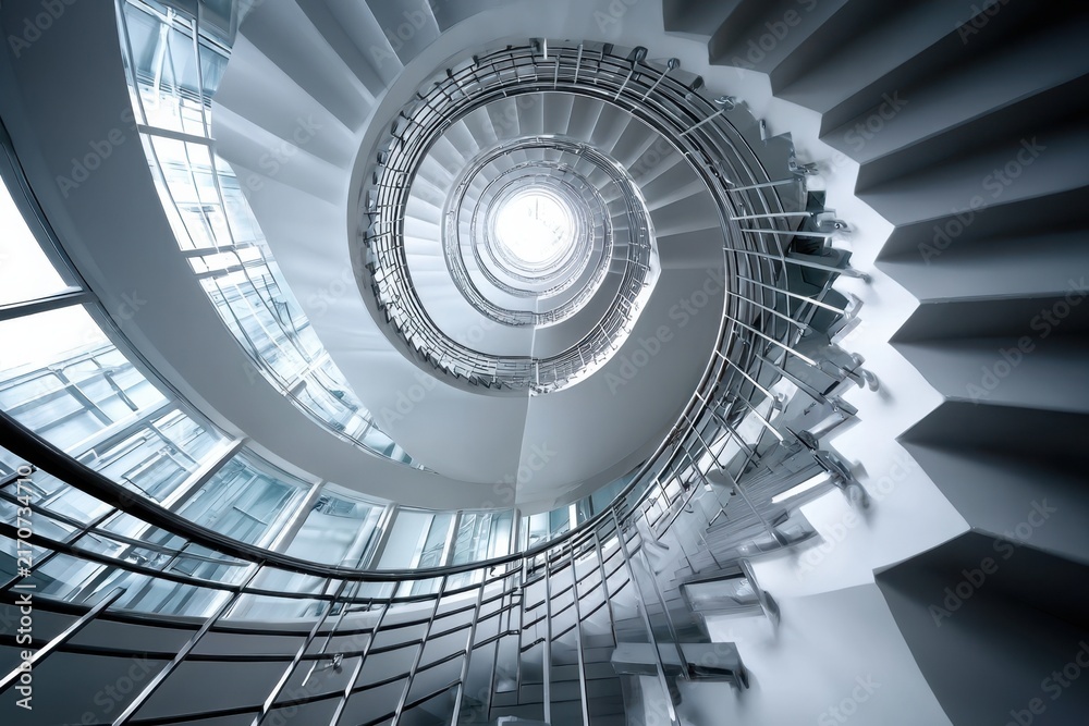 Fototapeta premium Modern white spiral staircase with metal railings in a bright building interior