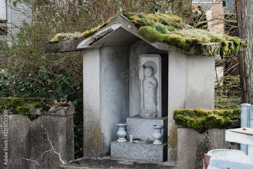 Принти на полотні Stone Buddhist Statue Enshrined in a Moss Covered Roadside Shrine