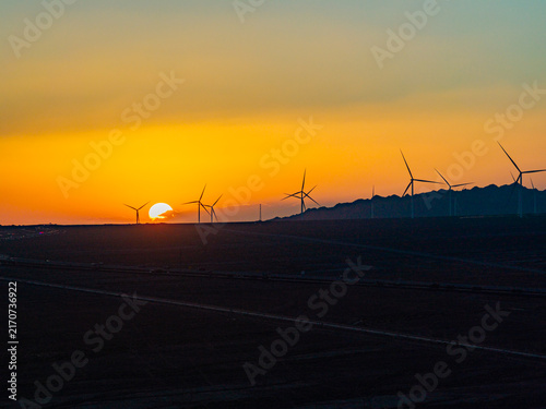 Solar photovoltaic panels at sunrise/sunset; wind turbine power plant; new energy