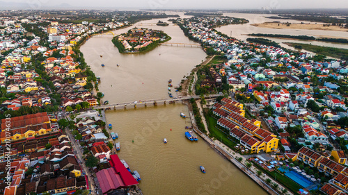 Aerial view of Hoi An with its iconic yellow buildings, traditional bridges, and boats navigating the Thu Bon River in Hoi An, Da Nang, Vietnam.