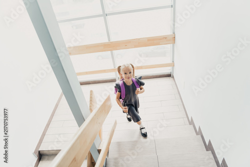 Konstfotografi Young schoolgirl with backpack climbing bright stairwell on her way to school, s