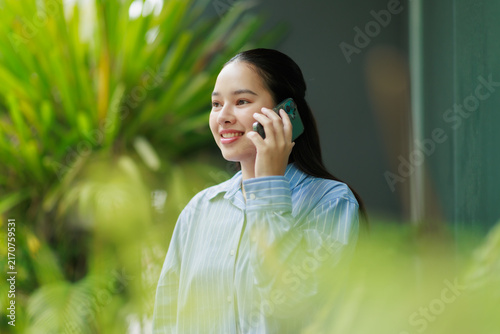 Canvastavla Young smiling Asian woman communicating with smartphone, enjoying a pleasant con