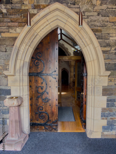 Fotografía Ornate wooden church door standing open within a pointed Gothic stone arch, with the historic interior visible beyond the entrance