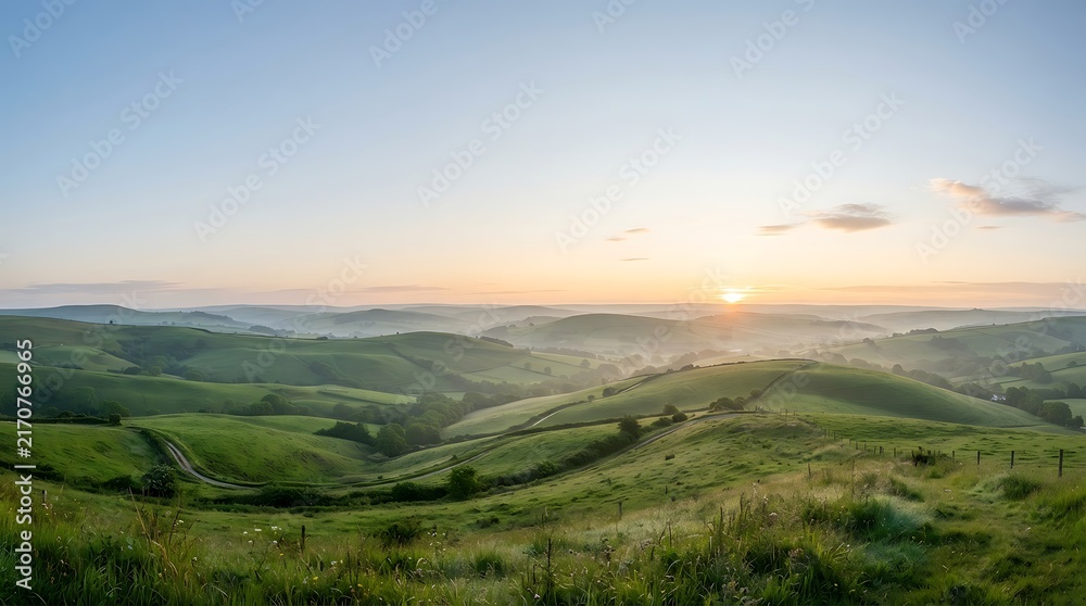 Fototapeta premium Sunrise over green rolling hills and misty valley landscape at dawn