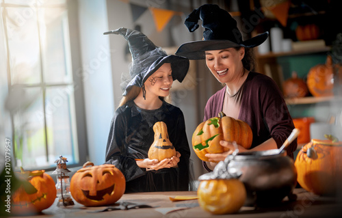 Happy Mother and Daughter in Witch Costumes Carving Pumpkins