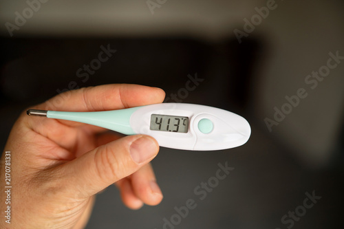 Close-up of hand holding a digital thermometer at home. concept: healthcare, illness, and monitoring temperature.