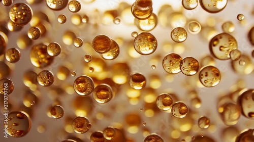 Golden liquid bubbles float and drift slowly in a warm blurred background. Animated scene combines spherical bubbles and liquid droplets with glowing light.