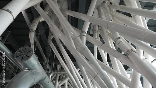 Intricate network of white pipes and metal tubes inside a modern industrial flour mill, showcasing the complex machinery and automated system for grain processing and food production
