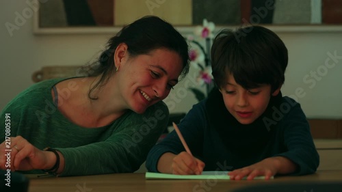 Smiling mother encourages her son as he completes a writing exercise at the family table, celebrating educational progress, shared learning and joyful connection