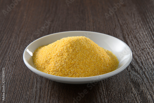 Fine golden cornmeal powder in a white ceramic bowl on a dark wooden table, shallow depth with natural diffused kitchen lighting