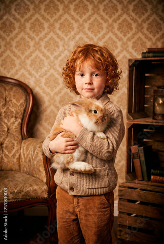 Red-haired child holding a ginger kitten in a vintage interior