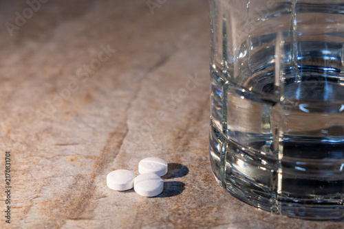 Konstfotografi Pills and Water Glass, Three white round pills are placed on a textured surface