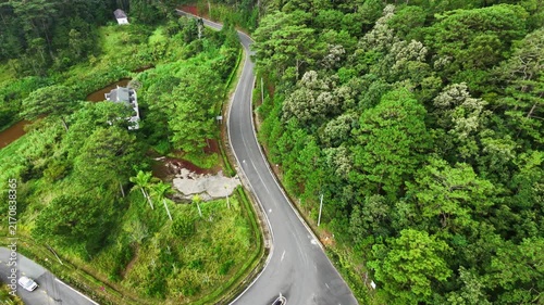 Aerial pan over winding forest road with cars driving through lush green landscape